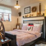 Spálňa s čiernou drevenou posteľou, posteľnou bielizňou s kvetinovým vzorom a veľkým kolovrátkom pri okne.