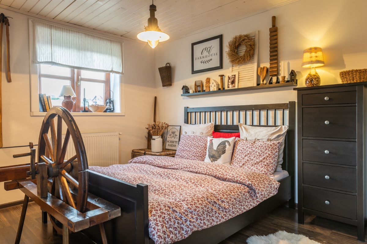 Spálňa s čiernou drevenou posteľou, posteľnou bielizňou s kvetinovým vzorom a veľkým kolovrátkom pri okne.