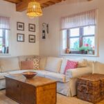 Rohová biela sedacia súprava, drevená truhlica ako konferenčný stolík a prútený kôš v obývačke s trámovým stropom.