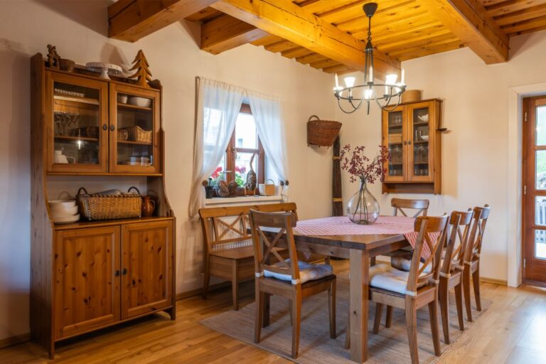 Jedáleň s dreveným stolom a stoličkami, masívnou drevenou komodou a dreveným trámovým stropom v rustikálnom štýle.