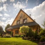 Drevený zrubový dom s čiernou strechou a vonkajším posedením obklopený záhradou a zeleňou.