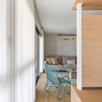 Svetlý moderný interiér s drevenou podlahou, béžovou pohovkou a tyrkysovým dizajnovým kreslom pri okne.