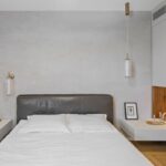 Spálňa s bielou posteľou, sivým koženým čelom, dreveným lamelovým obkladom a minimalistickými nočnými stolíkmi.