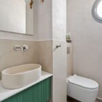 Moderná toaleta so sivými betónovými stenami, zelenou lamelovou skrinkou a kameninovým umývadlom.