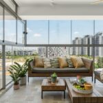 Presklená terasa s tmavým dreveným záhradným nábytkom, vankúšmi a výhľadom na mestské budovy.