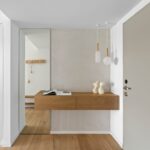 Vstupná hala s drevenou konzolou, veľkým zrkadlom a dvoma závesnými svietidlami na betónovej stene.