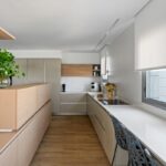 Lineárna moderná kuchyňa so svetlým drevom, bielymi pultmi a krémovými skrinkami v neutrálnom odtieni.