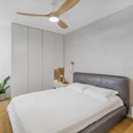 Moderná spálňa so sivou koženou posteľou, vstavanými skriňami a dreveným stropným ventilátorom.