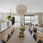 Otvorená dispozícia obývačky a jedálne so svetlým drevom, zamatovou pohovkou a veľkým papierovým tienidlom.