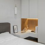 Biela spálňa so sivým koženým čelom, minimalistickým nočným stolíkom a svetlosivou vstavanou skriňou.