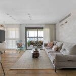 Svetlá obývačka s béžovou pohovkou, drevenou podlahou a sivou betónovou stenou.