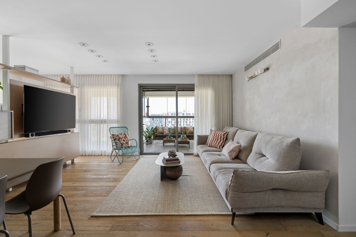 Svetlá obývačka s béžovou pohovkou, drevenou podlahou a sivou betónovou stenou.