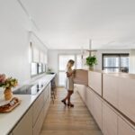 Minimalistická kuchyňa so svetlým dreveným ostrovčekom, krémovými skrinkami a dlhou bielou pracovnou doskou.