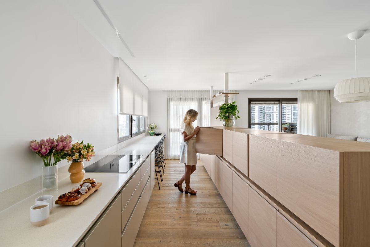 Minimalistická kuchyňa so svetlým dreveným ostrovčekom, krémovými skrinkami a dlhou bielou pracovnou doskou.