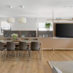 Otvorený vzdušný priestor s jedálenským stolom, dreveným obkladom a integrovanou kuchynskou linkou v neutrálnych farbách.