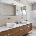 Moderná kúpeľňa s dvojitým umývadlom, drevenou skrinkou s lamelovým vzorom a veľkým zrkadlom.