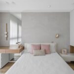 Spálňa s bielou posteľou, ružovými vankúšmi, dreveným toaletným stolíkom a betónovou sivou stenou.