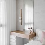 Biely toaletný stolík s drevenou vrchnou doskou, zvislým zrkadlom a nástennou lampou s dreveným podkladom.