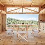 Interiér mobilného domu zo svetlého dreva so stolom, stoličkami a otvorenou stenou do prírody,