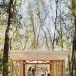 Otvorený mobilný dom s drevenou konštrukciou a bielou látkovou strechou v lese.