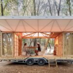 Otvorený drevený interiér mobilného domu v lese, so slnečným posedením pre dvoch.