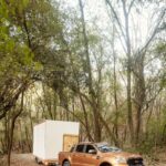 Mobilný dom s bielou fasádou na prívese, ťahanom hnedým pick-upom