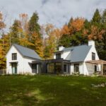 Moderný biely dom s tmavou prístavbou a šedou plechovou strechou.