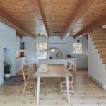 Jedáleň a kuchyňa s dreveným trámovým stropom, bielou kuchynskou linkou, drevenou skriňou a schodmi na poschodie.