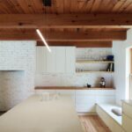 Biela kuchyňa s drevenou pracovnou doskou a otvorenými policami, s bielym tehlovým murivom a drevenými trámami na strope.
