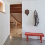 Vstupný priestor s červenou lavičkou, vešiakmi na stene a priechodom do dennej miestnosti s drevenou podlahou.