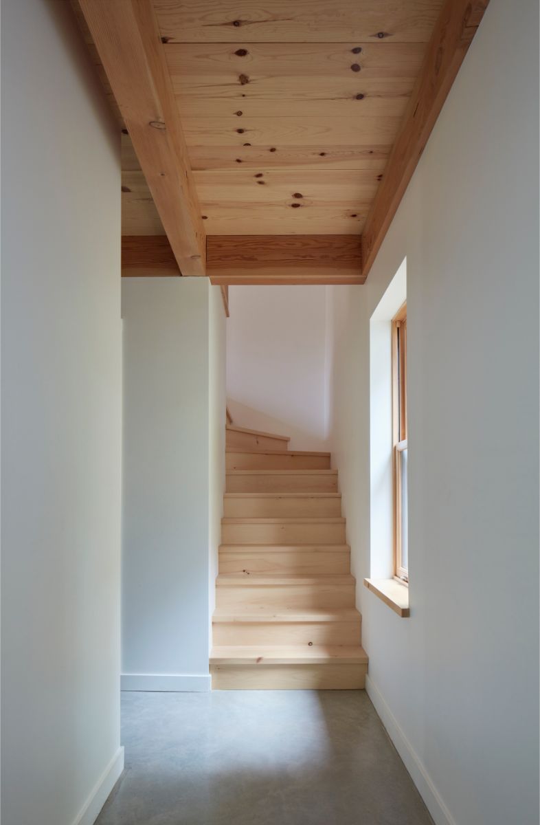 Schody s drevenou nášľapnou plochou, bielymi stenami a dreveným trámovým stropom.