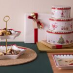 Vianočné plechové dózy s červeno-bielym dekorom a dvojposchodový etažér s vianočným pečivom na drevenom stole.