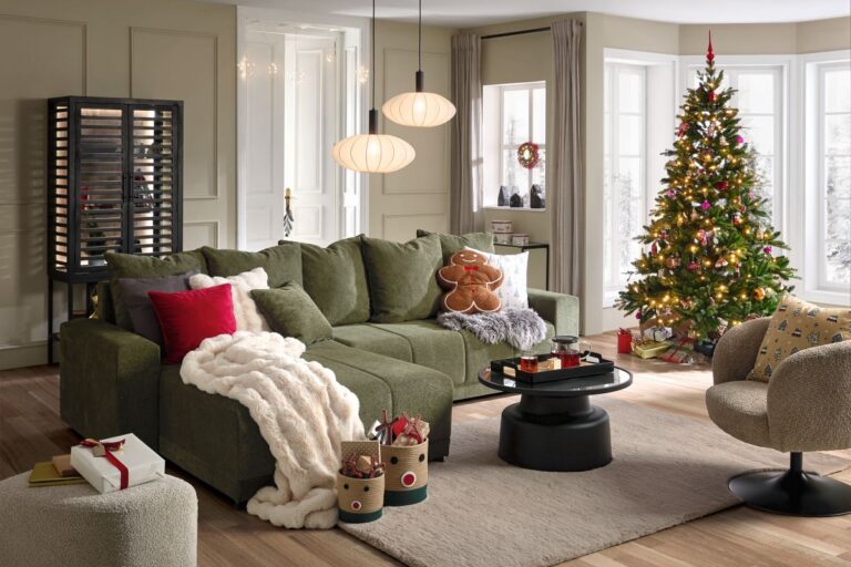 Priestor obývačky s veľkou tmavozelenou rohovou sedačkou, svetlým kobercom a tradičným vianočným stromčekom s farebnými ozdobami.