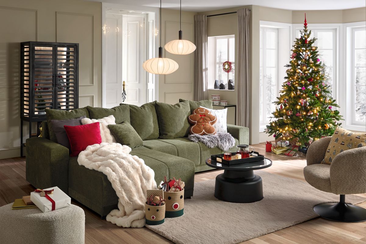 Priestor obývačky s veľkou tmavozelenou rohovou sedačkou, svetlým kobercom a tradičným vianočným stromčekom s farebnými ozdobami.