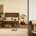 Svetlá spálňa s bielou stenou, ratanovou posteľou, dreveným nábytkom a béžovým kobercom na parketách.