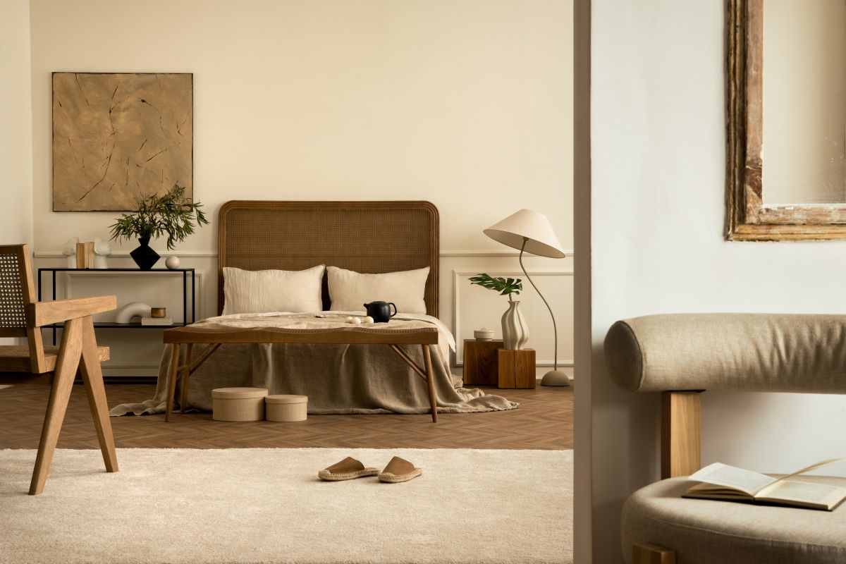 Svetlá spálňa s bielou stenou, ratanovou posteľou, dreveným nábytkom a béžovým kobercom na parketách.