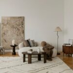 Obývačka v neutrálnych tónoch s bielou bouclé sedačkou, abstraktným obrazom a okrúhlym dreveným konferenčným stolíkom.