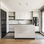Moderná kuchyňa v kombinácii bielej a sivej farby, s kamenným ostrovčekom, čiernou chladničkou a drevenou podlahou.