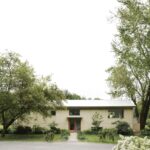 Svetlý moderný dom s veľkými oknami, drevenou fasádou a vstupom v objatí stromov.