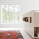 Svetlá spálňa s veľkým oknom do lesa, drevenou podlahou a dizajnovým oranžovým kobercom.