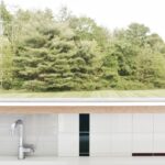 Biely kuchynský pult s chrómovou batériou a okenným výhľadom na les.