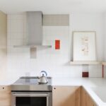 Minimalistická kuchyňa s bielym obkladom, drevenými skrinkami a digestorom z nehrdzavejúcej ocele.