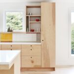 Moderná kuchynská linka z brezovej preglejky, biely obklad a veľké okno s výhľadom do zelene.