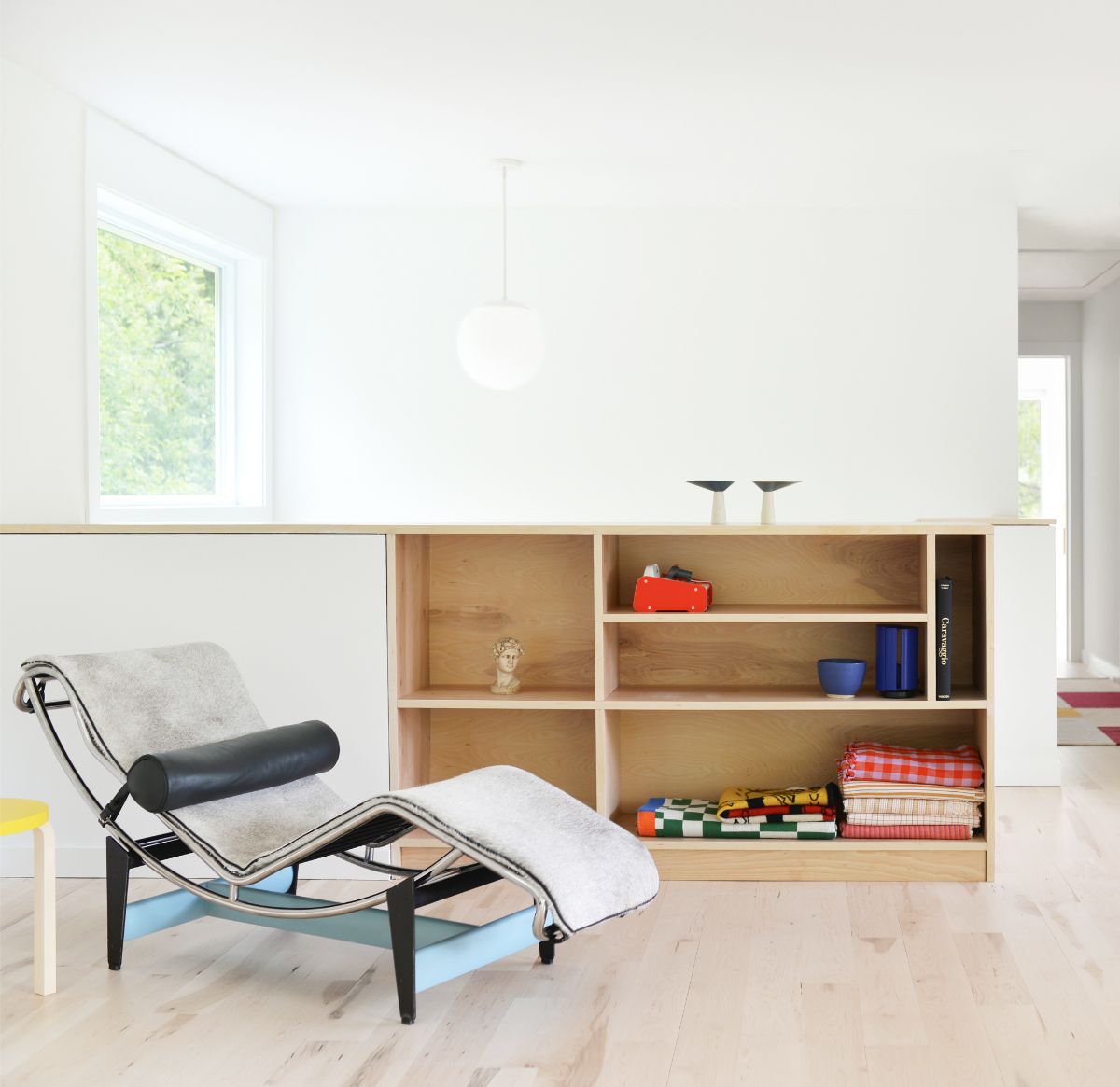 Svetlý priestor s drevenou podlahou, nízkou úložnou skrinkou a ležadlom v štýle mid-century modern.