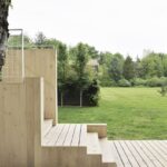 Rohový drevený vstup s drevenými schodmi na terasu v trávnatom sade.