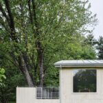 Drevená fasáda domu a terasa s bielou mriežkovou zábranou a veľkým oknom s odrazom stromu.