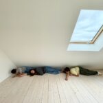 Trojčlenná rodina leží v prázdnom podkrovnom priestore na podlahe zo svetlého dreva.