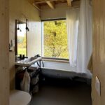 Kúpeľňa s dreveným obkladom, umývadlom, toaletou a vaňou pri veľkom okne.