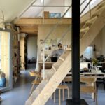 Interiér s drevenou stenou, schodiskom, stĺpom kachlí a jedálenským kútom,