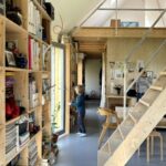 Dieťa stojí pri presklených dverách v interiéri s vysokými drevenými regálmi, schodiskom a drevenou galériou.